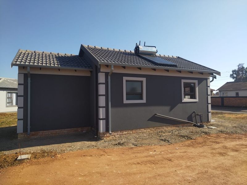 Rear view of a modern house featuring a dark grey facade, tiled roof, and an installed solar water heating system.