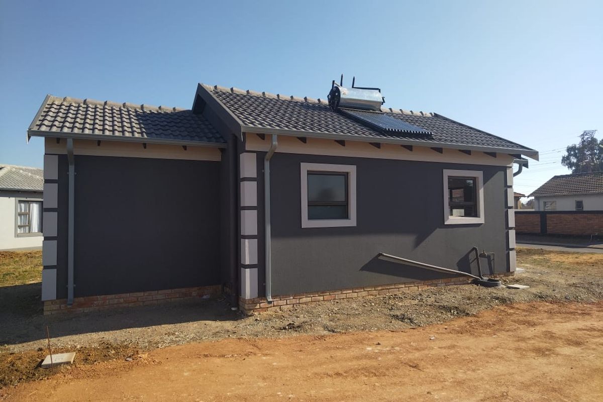 Rear view of a modern house featuring a dark grey facade, tiled roof, and an installed solar water heating system.
