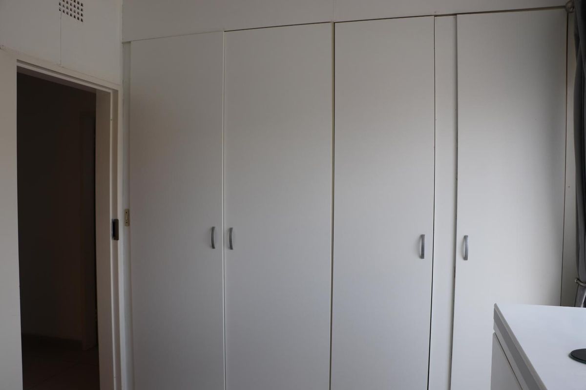 A bedroom featuring built-in floor-to-ceiling white cabinetry with modern handles, providing ample storage space.