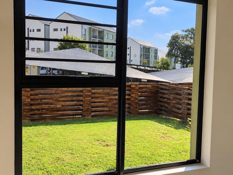A bright, empty bedroom featuring a large black aluminium window with security bars, overlooking a private garden area.