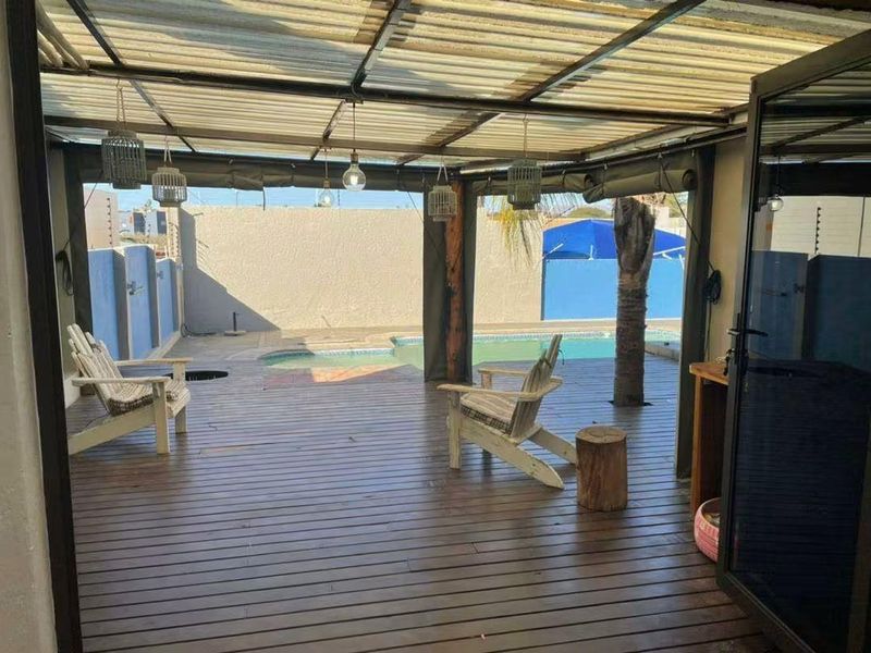 Covered outdoor patio featuring timber decking, overlooking a private swimming pool and enclosed garden area.