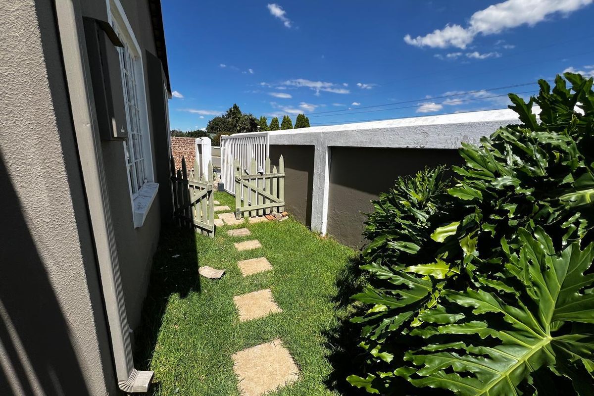 A side garden pathway featuring a grass lawn, stone pavers, and a secure boundary wall with a timber gate.
