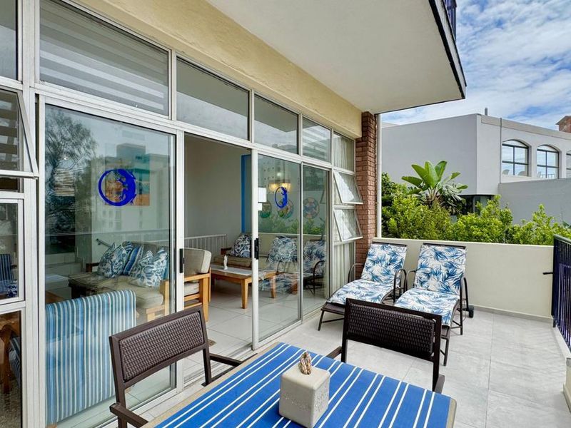 A spacious covered balcony featuring tiled flooring, metal railings, and large sliding glass doors providing seamless access to the interior living area.