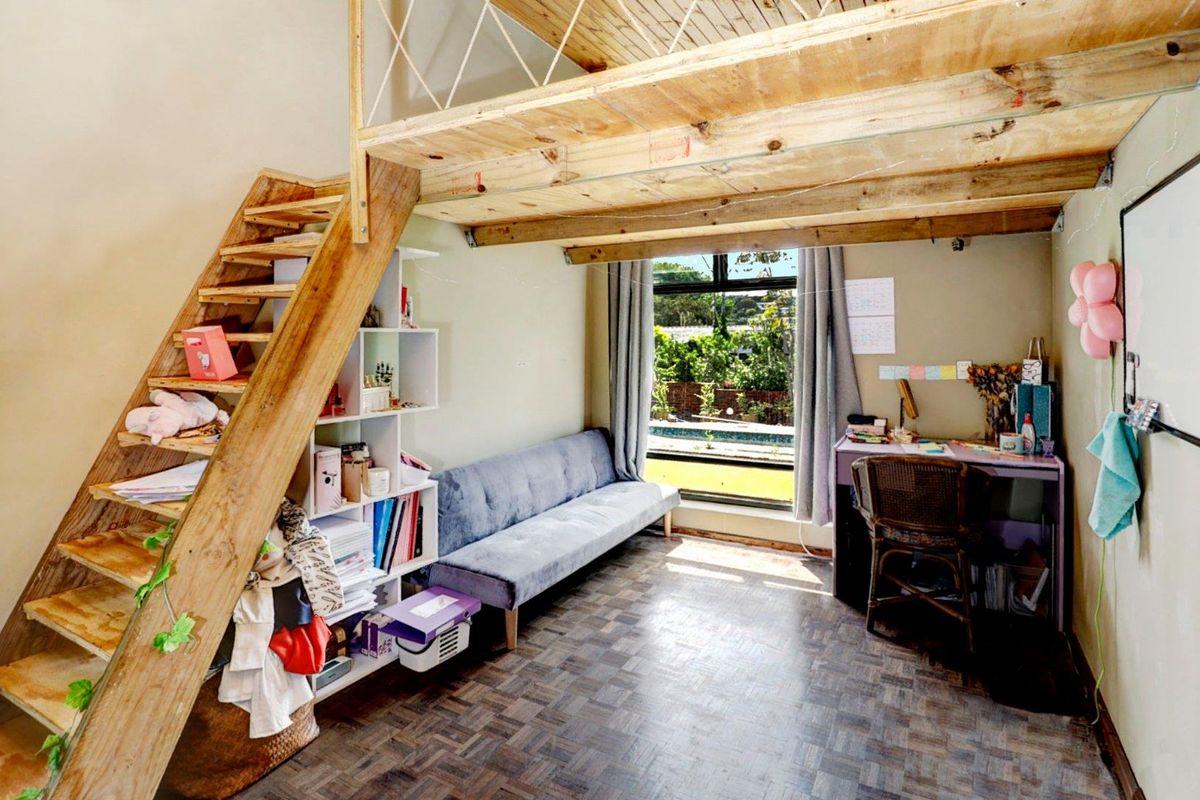 A versatile bedroom featuring a built-in timber loft sleeping area, accessible via a wooden staircase, with parquet flooring and garden views.