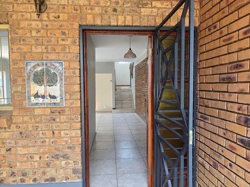 Entrance area featuring exposed brickwork, a security gate, and tiled flooring leading to an internal staircase.