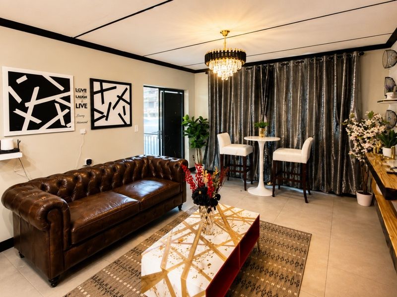 A well-maintained living room featuring tiled flooring, modern ceiling lighting, and a chandelier, with an adjacent bedroom visible.