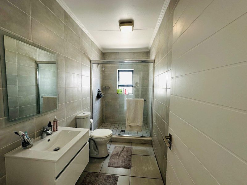 A modern bathroom featuring a vanity cabinet, toilet, and a glass-enclosed shower with neutral wall and floor tiling.