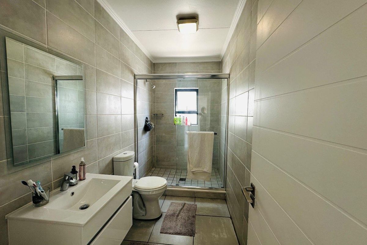 A modern bathroom featuring a vanity cabinet, toilet, and a glass-enclosed shower with neutral wall and floor tiling.