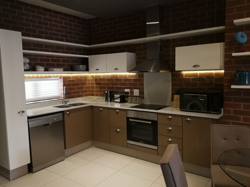 Modern kitchen featuring exposed brick walls, sleek cabinetry, quartz countertops, integrated appliances, and stylish under-cabinet lighting for a contemporary industrial aesthetic.