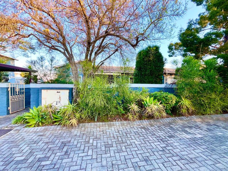 Front exterior view of the townhouse featuring a paved driveway, boundary wall, and gated pedestrian entrance with established garden landscaping.