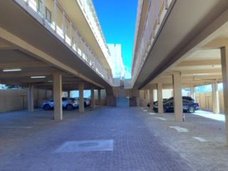 A covered ground-level parking area featuring concrete pillars and paved flooring, situated beneath the apartment building structure.