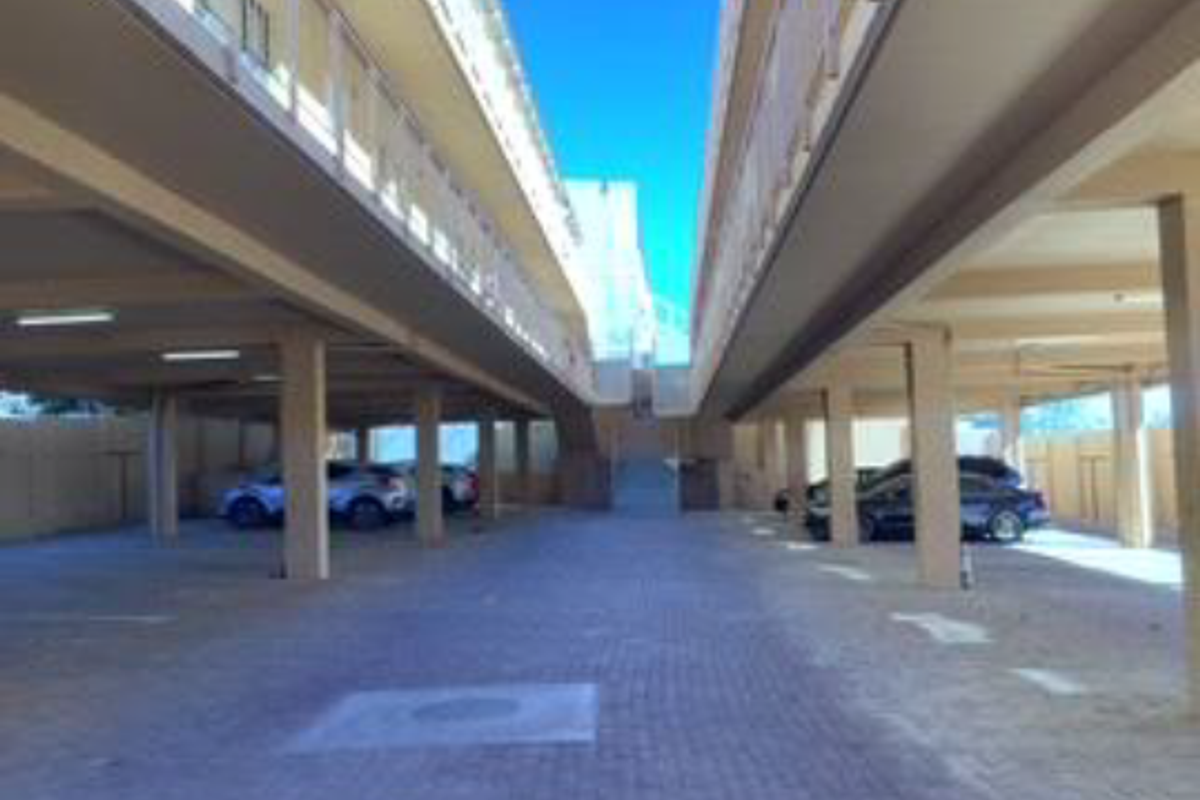 A covered ground-level parking area featuring concrete pillars and paved flooring, situated beneath the apartment building structure.