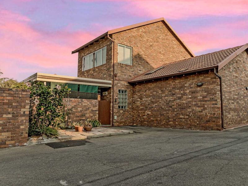 A well-maintained face brick townhouse exterior featuring a tiled roof, paved entrance area, and a distinctive glass block window detail.