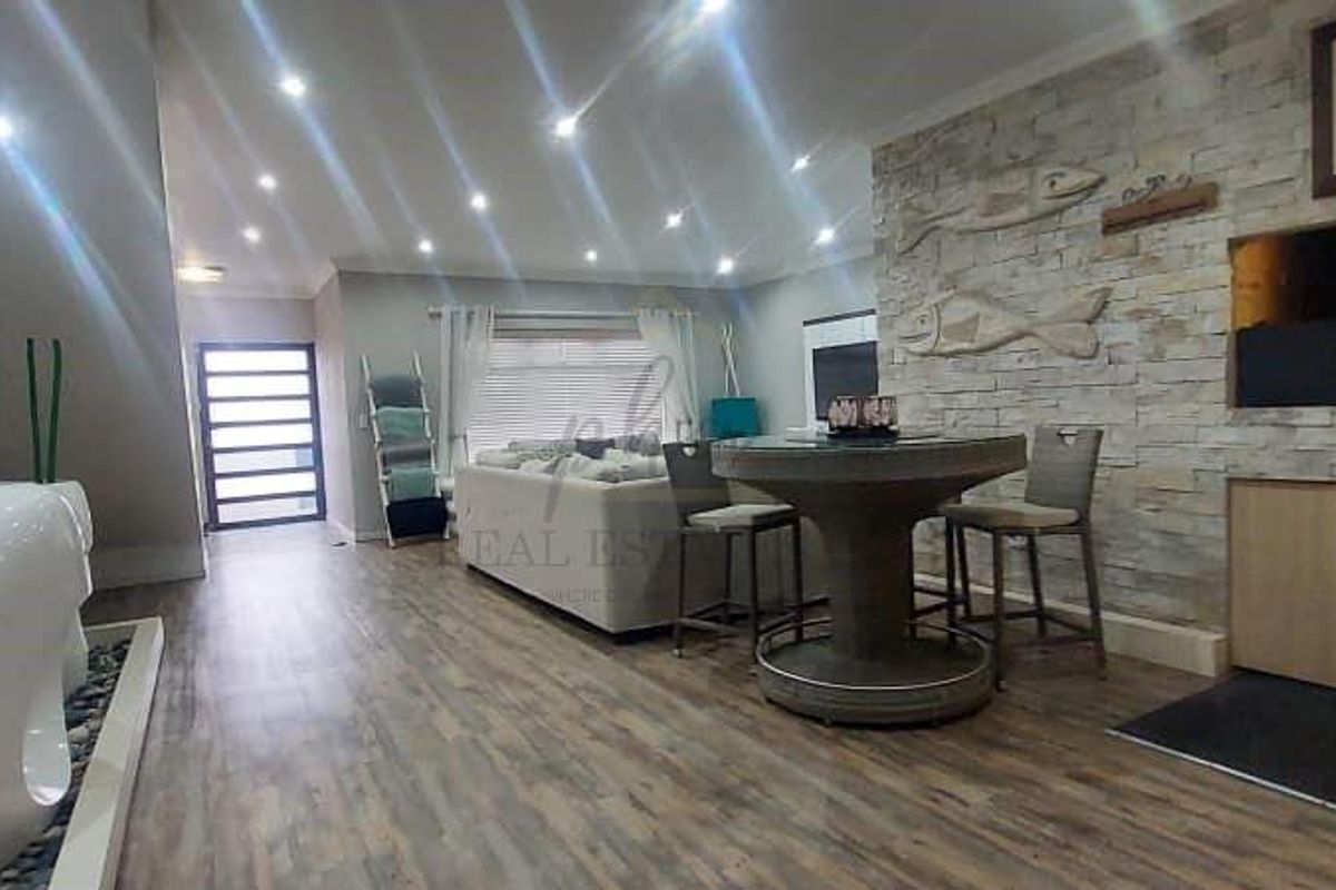 Spacious living area featuring a stone feature wall with a built-in fireplace, recessed downlighting, and modern laminate flooring.