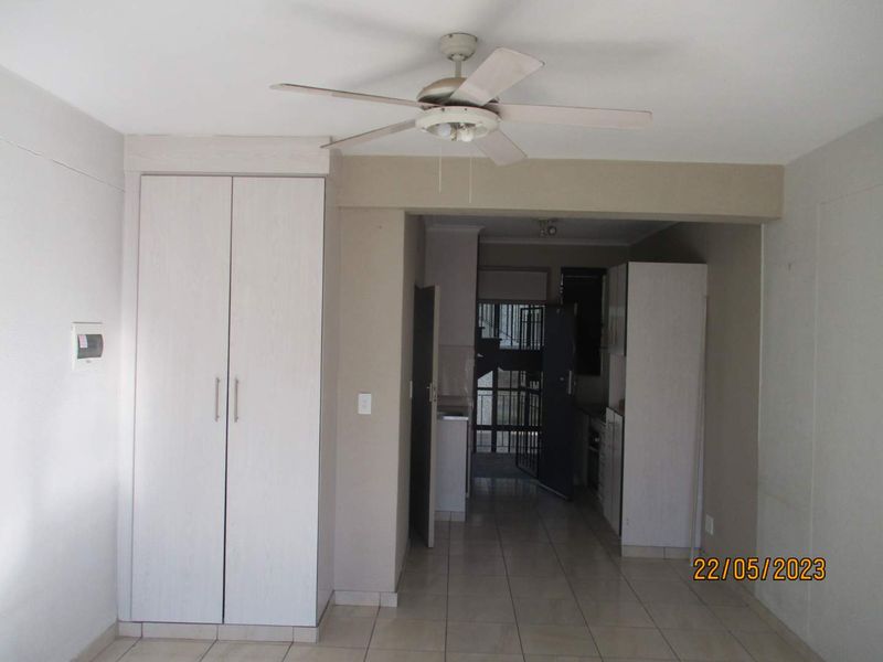 Open plan living area featuring tiled flooring, a ceiling fan, and built-in storage cupboards, leading towards a kitchen area with a security gate.