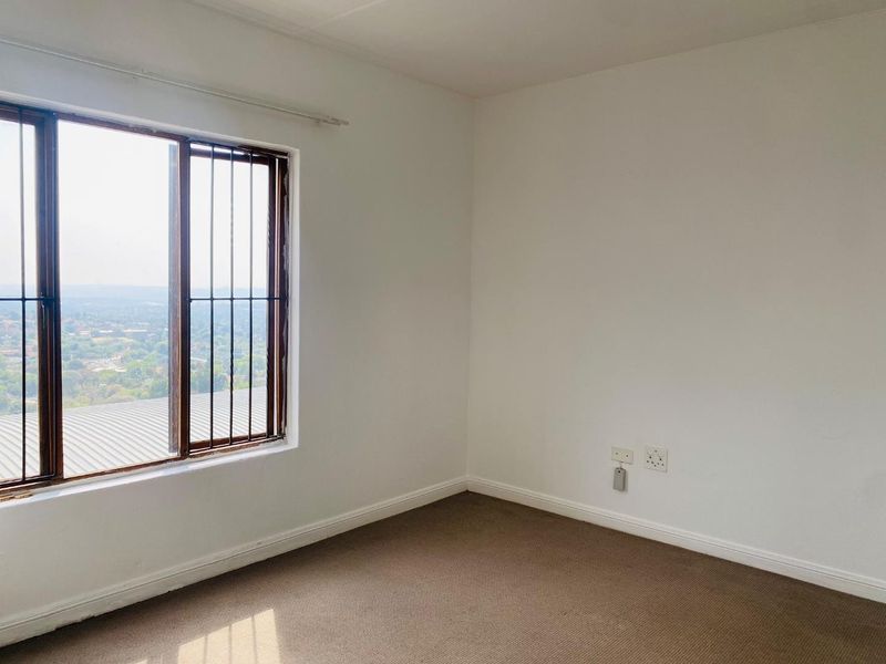 A bright, empty bedroom featuring carpeted flooring, neutral walls, and a window with security bars offering an elevated view.