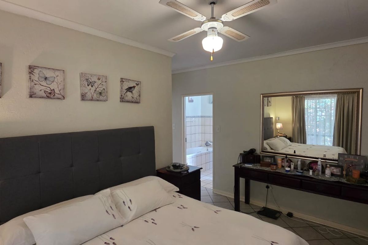 A comfortable bedroom featuring tiled flooring, a ceiling fan, and direct access to an en-suite bathroom.