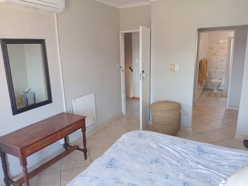A bedroom featuring tiled flooring, a wall-mounted air conditioning unit, and direct access to an en-suite bathroom.