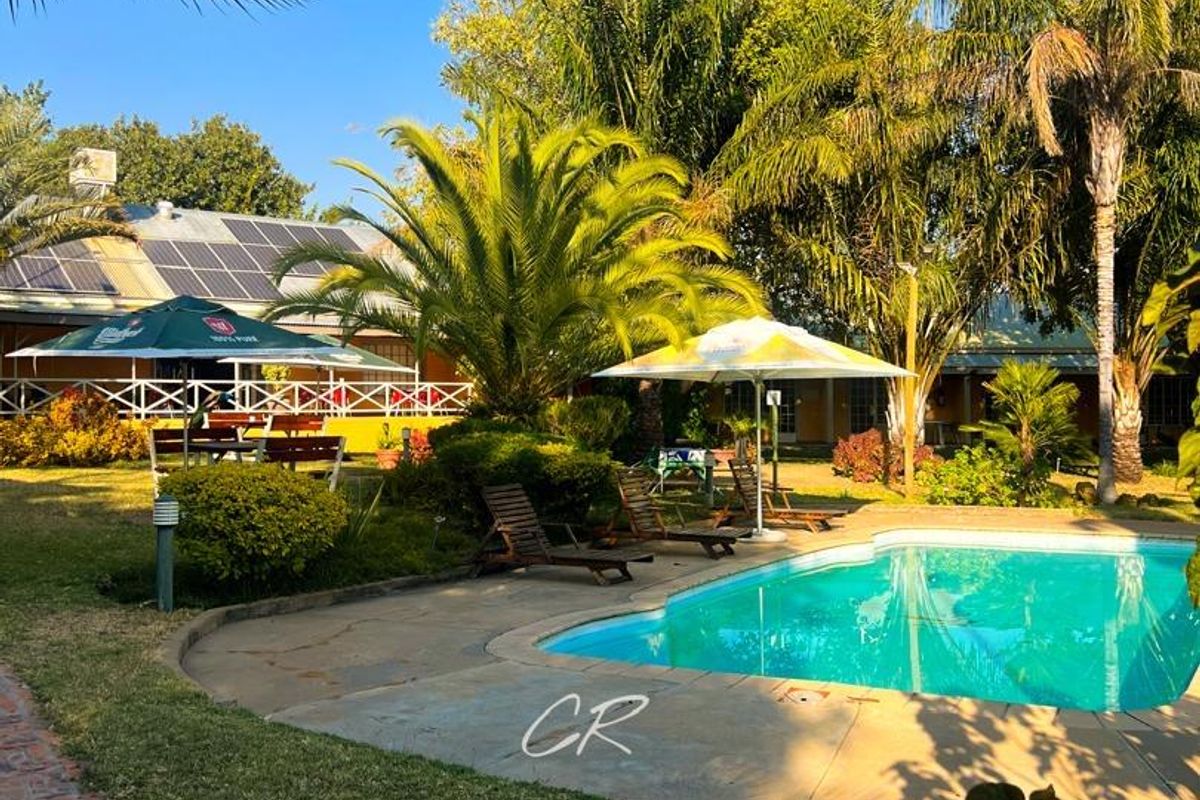 Outdoor pool area featuring a swimming pool, landscaped garden, and paved walkways, with solar panels visible on the building roof.