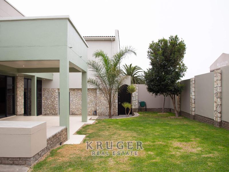 A well-maintained rear garden featuring a covered patio with stone cladding accents, a lawn area, and secure boundary walls.