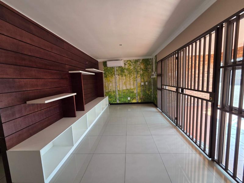 A bright, empty office space featuring tiled floors, built-in shelving, decorative wood-look wall paneling, and a secure metal gate entrance.