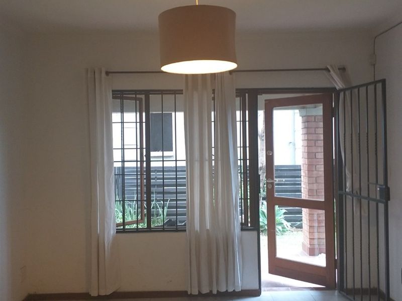 An empty living room featuring tiled flooring, a ceiling rose, and direct access to the exterior through a security gate and door.