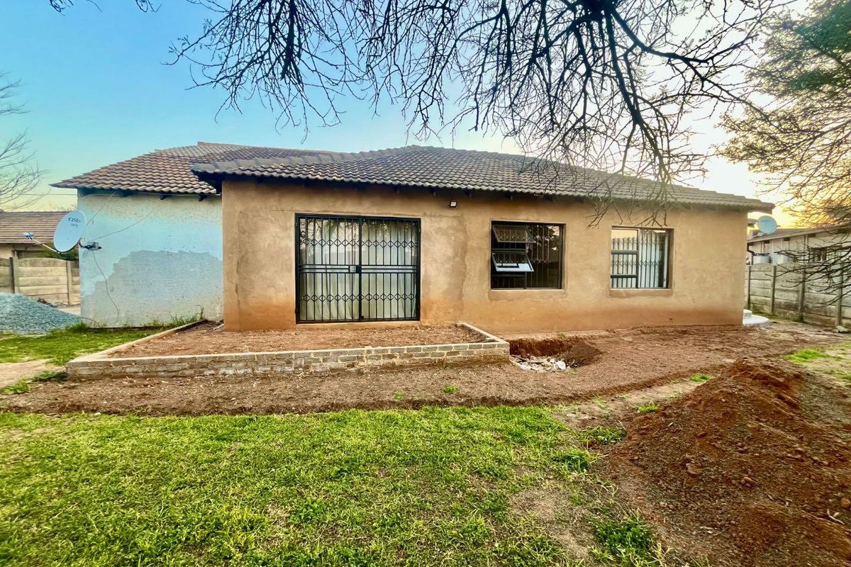 Rear view of the house featuring a tiled roof, security gates, and an unfinished garden area with a low brick retaining wall.