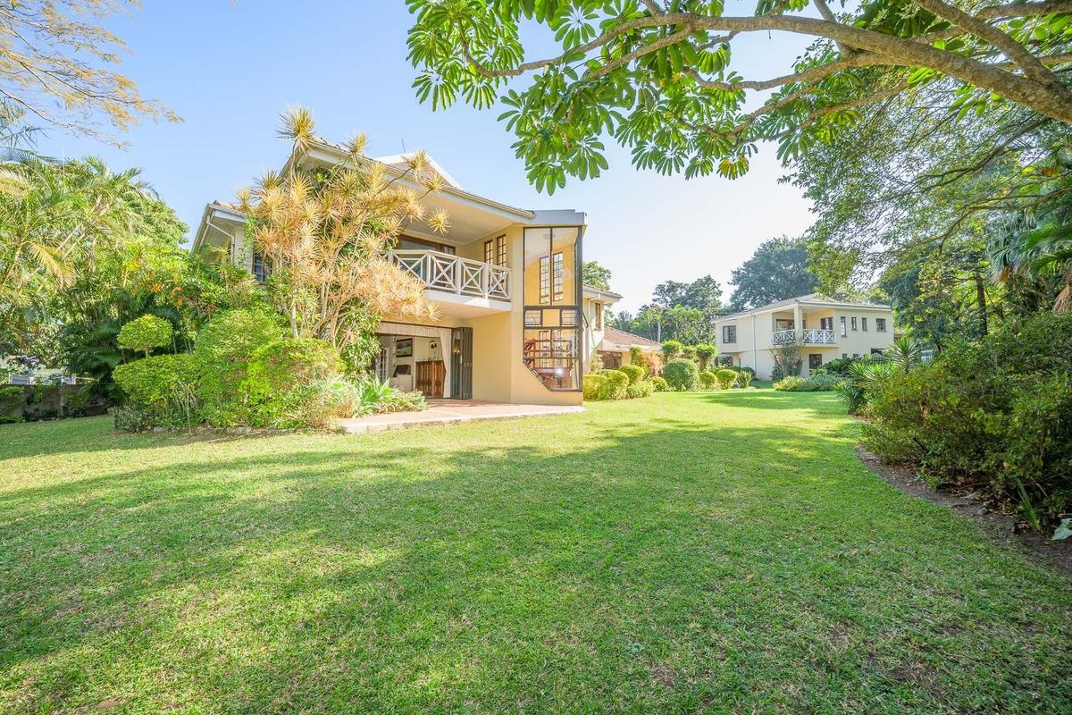 A spacious rear garden view featuring a multi-level home with a covered patio, balcony, and a distinctive spiral staircase design.