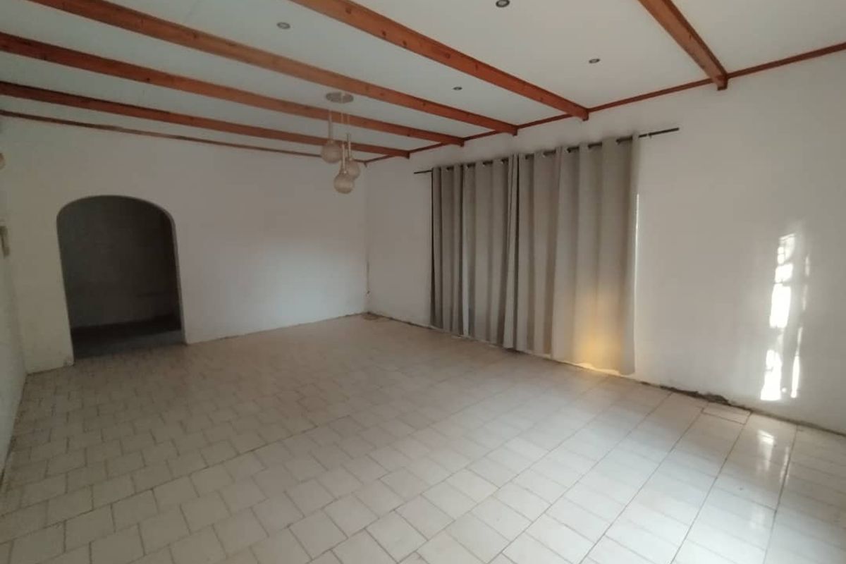 Spacious living area featuring exposed timber ceiling beams, tiled flooring, and an arched doorway leading to an adjacent room.