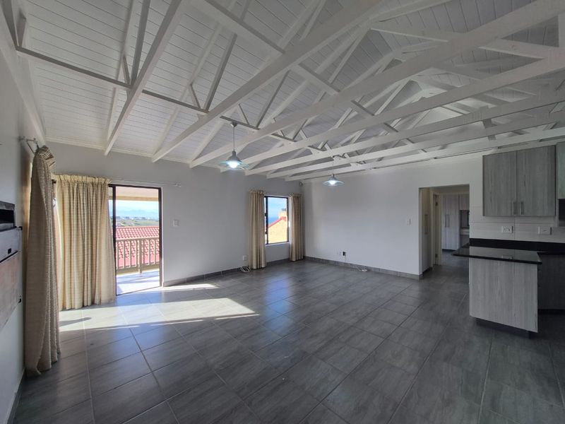 Spacious open-plan living area featuring exposed white timber trusses, tiled flooring, and a modern kitchen with granite countertops and direct balcony access.