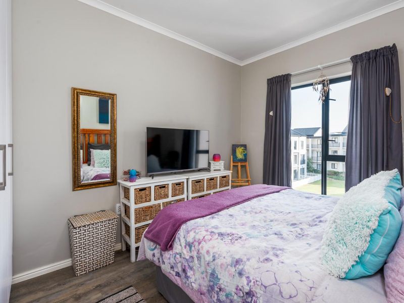 A well-maintained bedroom featuring laminate flooring, built-in wardrobes, and a large window providing natural light and views of the surrounding apartment complex.