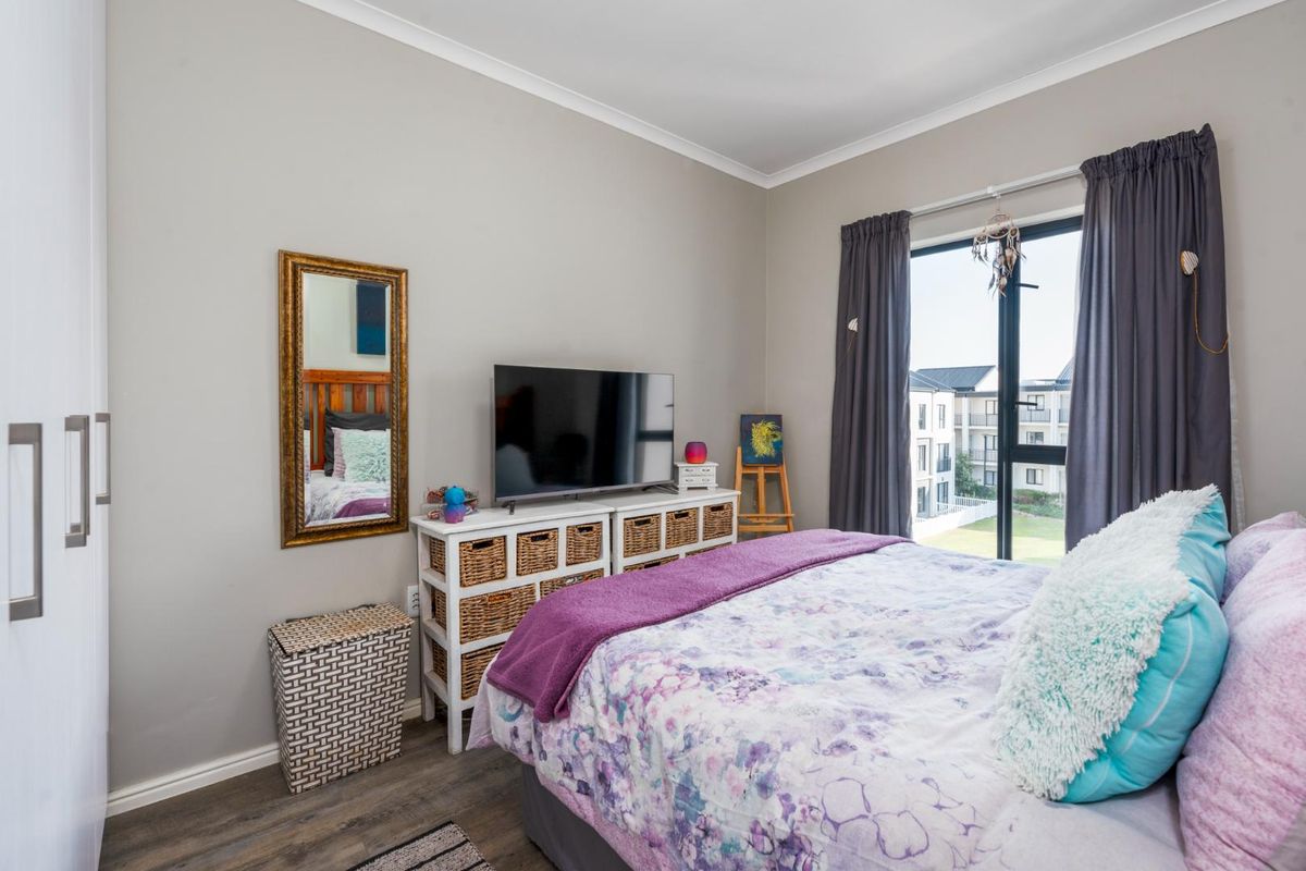 A well-maintained bedroom featuring laminate flooring, built-in wardrobes, and a large window providing natural light and views of the surrounding apartment complex.