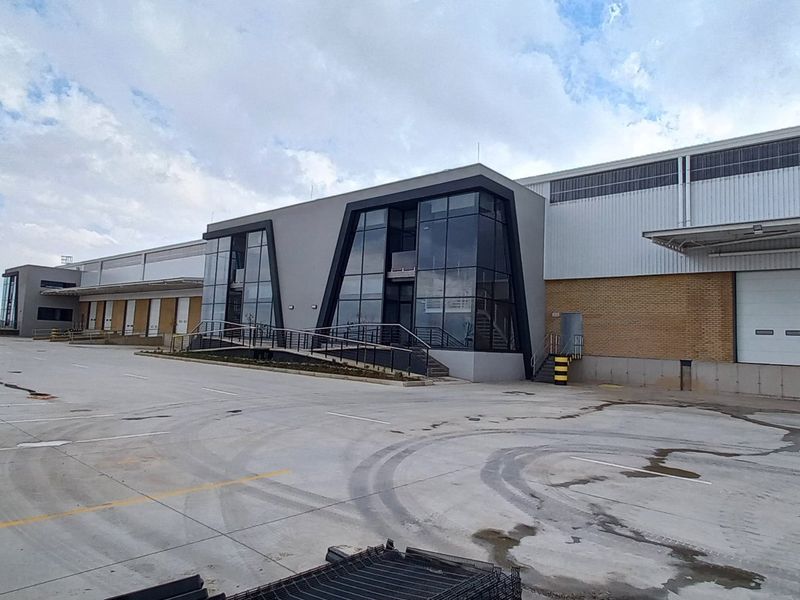 Modern industrial warehouse facility featuring extensive concrete hardstand, multiple loading docks with roller shutter doors, and a contemporary glass-fronted office entrance.