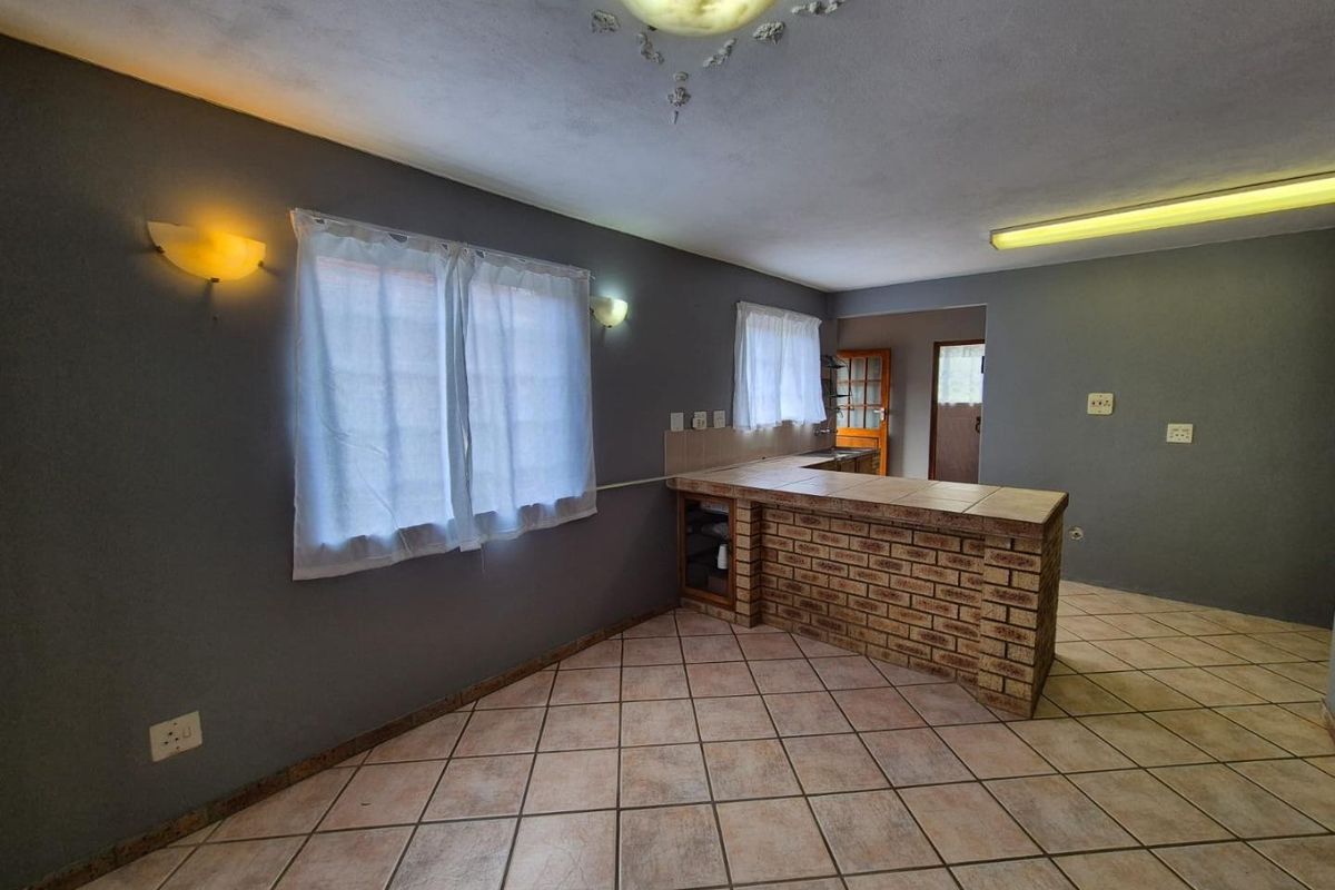 An empty kitchen area featuring a brick breakfast bar, tiled flooring, and tiled countertops, offering a blank canvas for modern renovation and design updates.