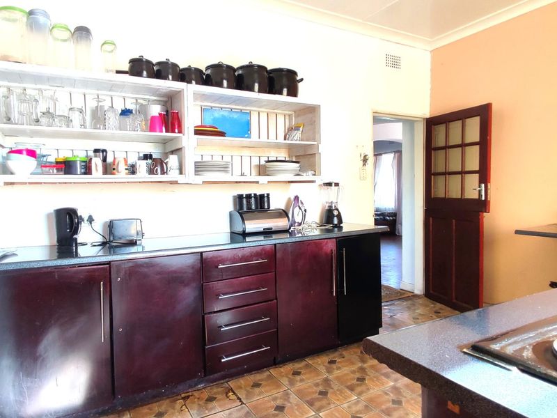 Kitchen featuring dark cabinetry, laminate countertops, open shelving, and tiled flooring, with a traditional timber door leading to an adjacent room.