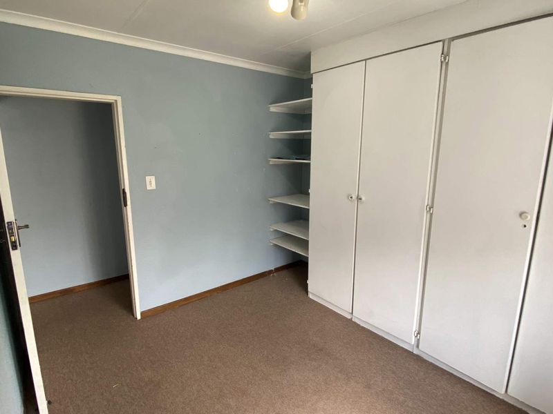 A vacant bedroom featuring built-in cupboards with integrated open shelving, neutral wall paint, and carpeted flooring.