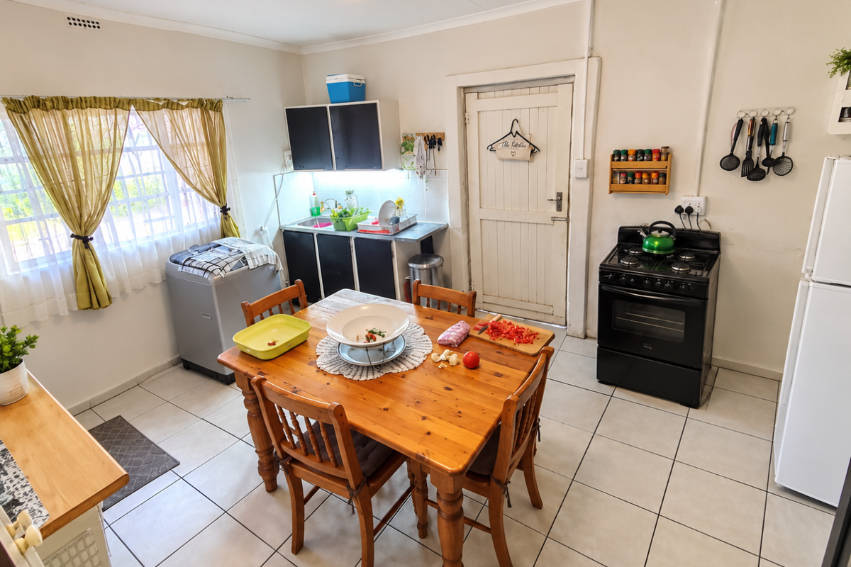A functional kitchen featuring tiled flooring, built-in cabinetry, a stainless steel sink, and a freestanding gas stove with an extractor fan.