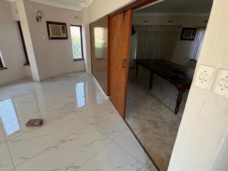 Spacious living area featuring polished porcelain tiles, crown molding, and a sliding wooden door connecting to an adjacent carpeted room.