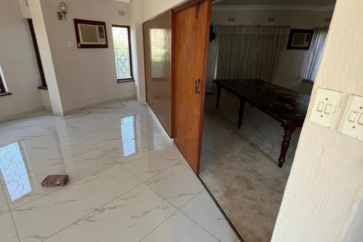 Spacious living area featuring polished porcelain tiles, crown molding, and a sliding wooden door connecting to an adjacent carpeted room.