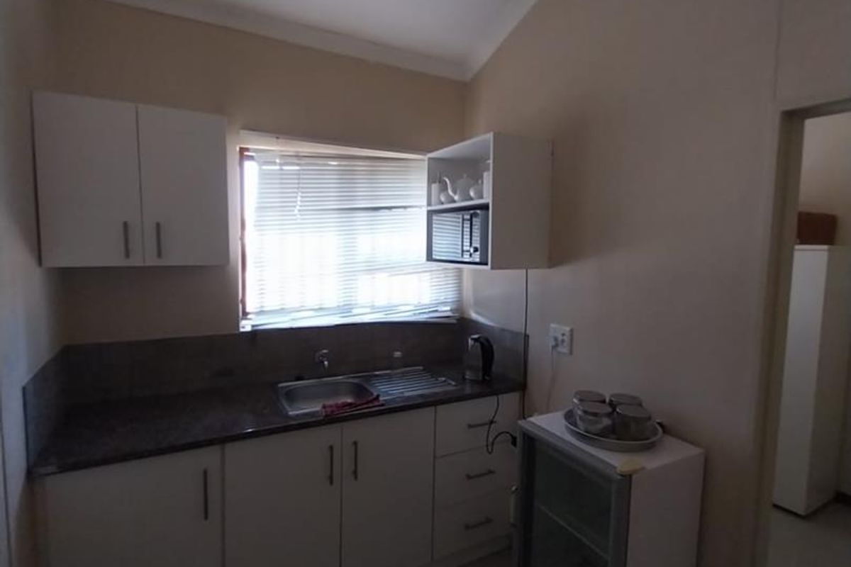 A compact kitchenette featuring white cabinetry, a dark countertop, a stainless steel sink, and tiled flooring.