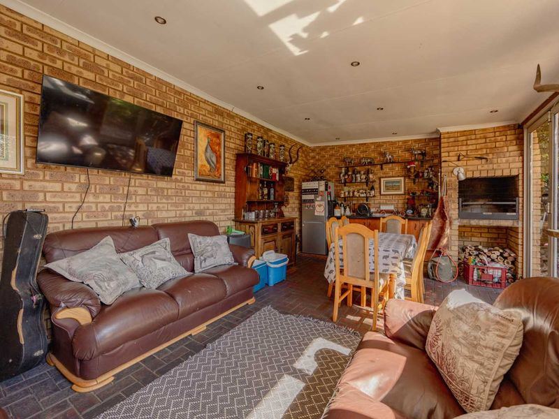 A spacious enclosed patio featuring exposed brick walls, a built-in braai, and paved flooring, offering a versatile entertainment area with direct access to the garden.