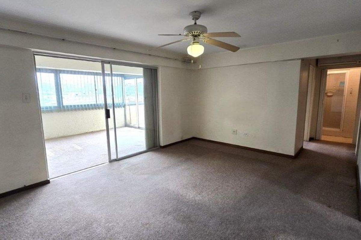 Spacious living area featuring a ceiling fan, carpeted flooring, and large sliding glass doors providing access to an enclosed balcony.