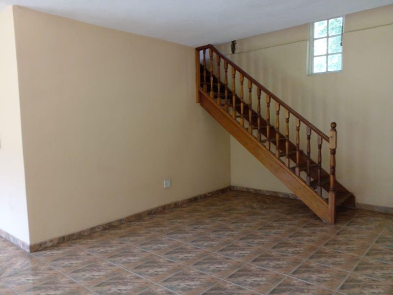 An empty living area featuring tiled flooring and a traditional wooden staircase leading to the upper level.