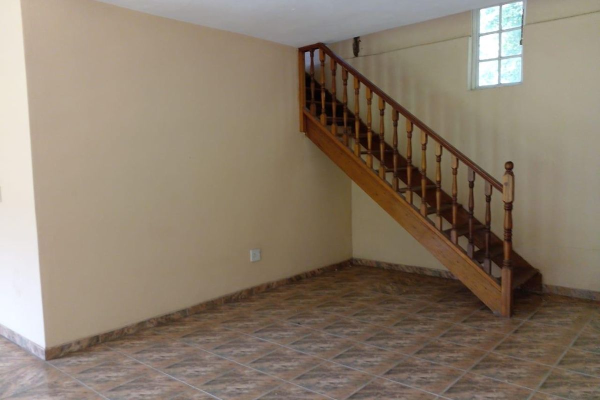An empty living area featuring tiled flooring and a traditional wooden staircase leading to the upper level.