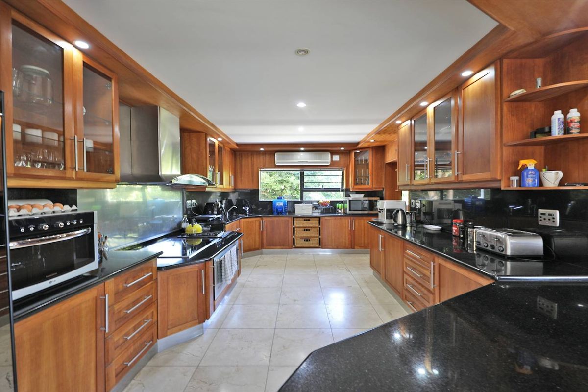 Spacious kitchen featuring extensive wooden cabinetry, black granite countertops, integrated oven, extractor fan, and tiled flooring.