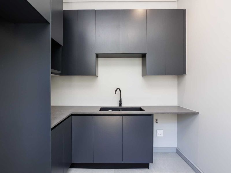 A modern, minimalist laundry area featuring dark grey cabinetry, a sleek matte black faucet, and a durable laminate countertop.