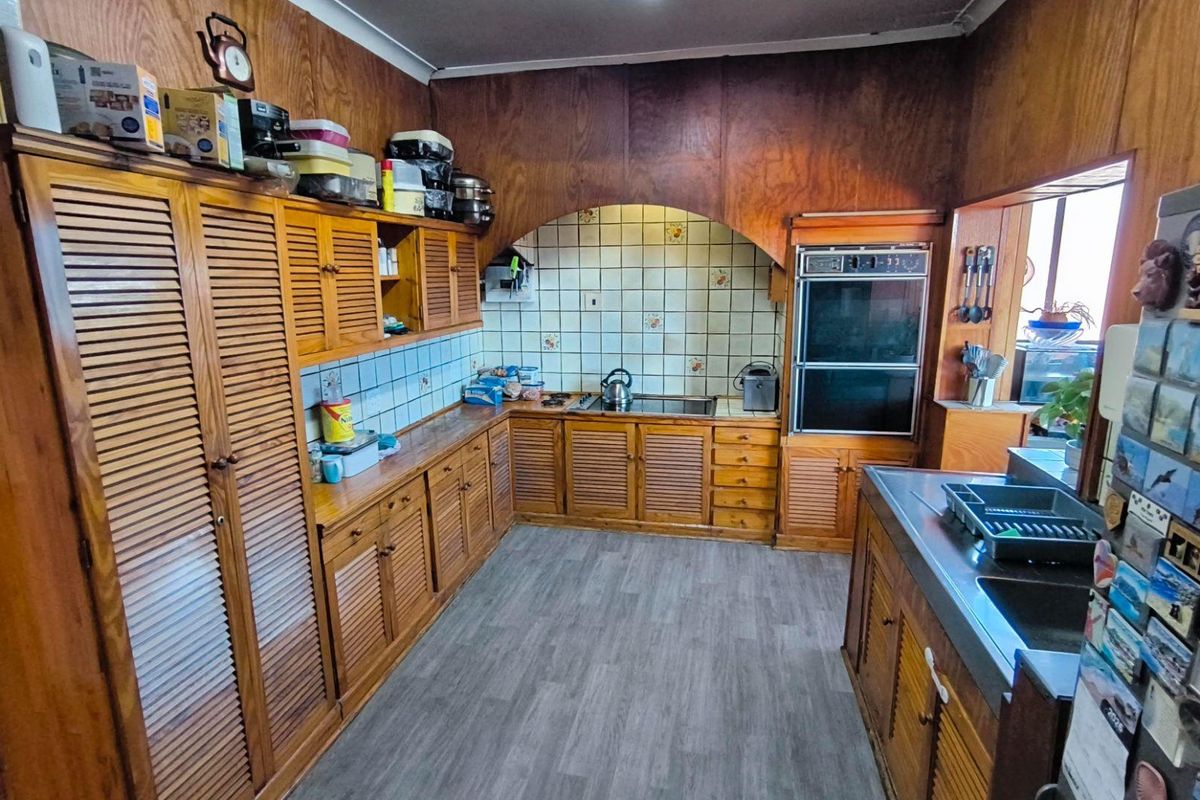 A dated kitchen featuring extensive wooden cabinetry, a built-in double oven, and a tiled backsplash, offering significant potential for a modern renovation.