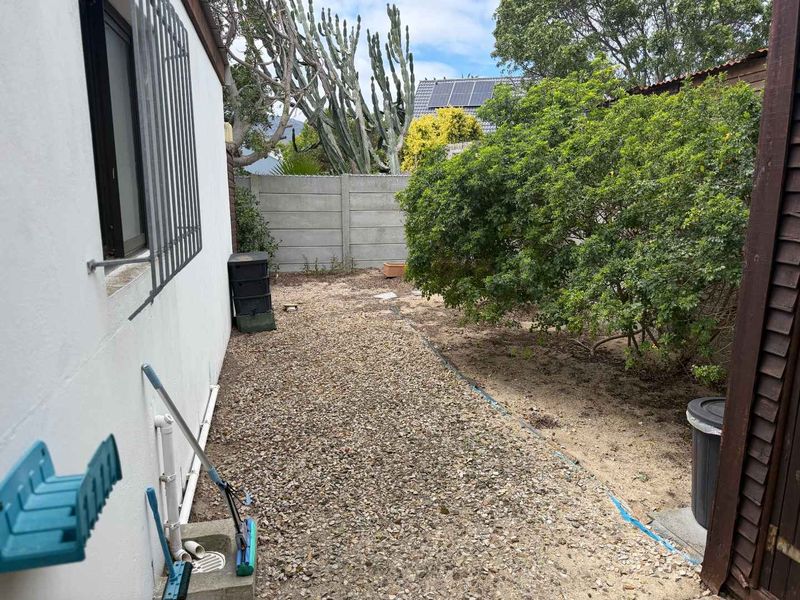 A rear exterior area featuring a gravel ground cover, precast concrete boundary wall, and security bars on the window.