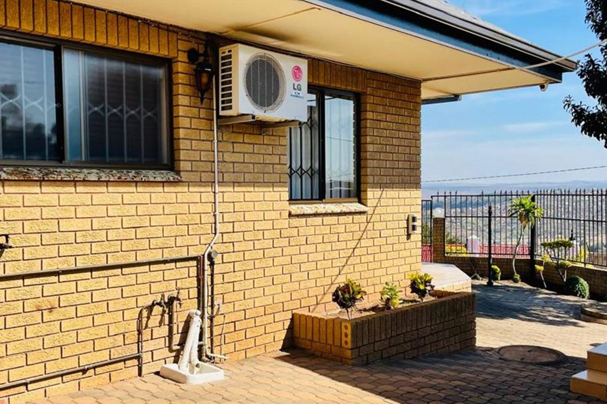 A rear exterior view featuring a paved patio area, brick facade, and an installed air conditioning unit with scenic views beyond the perimeter fence.
