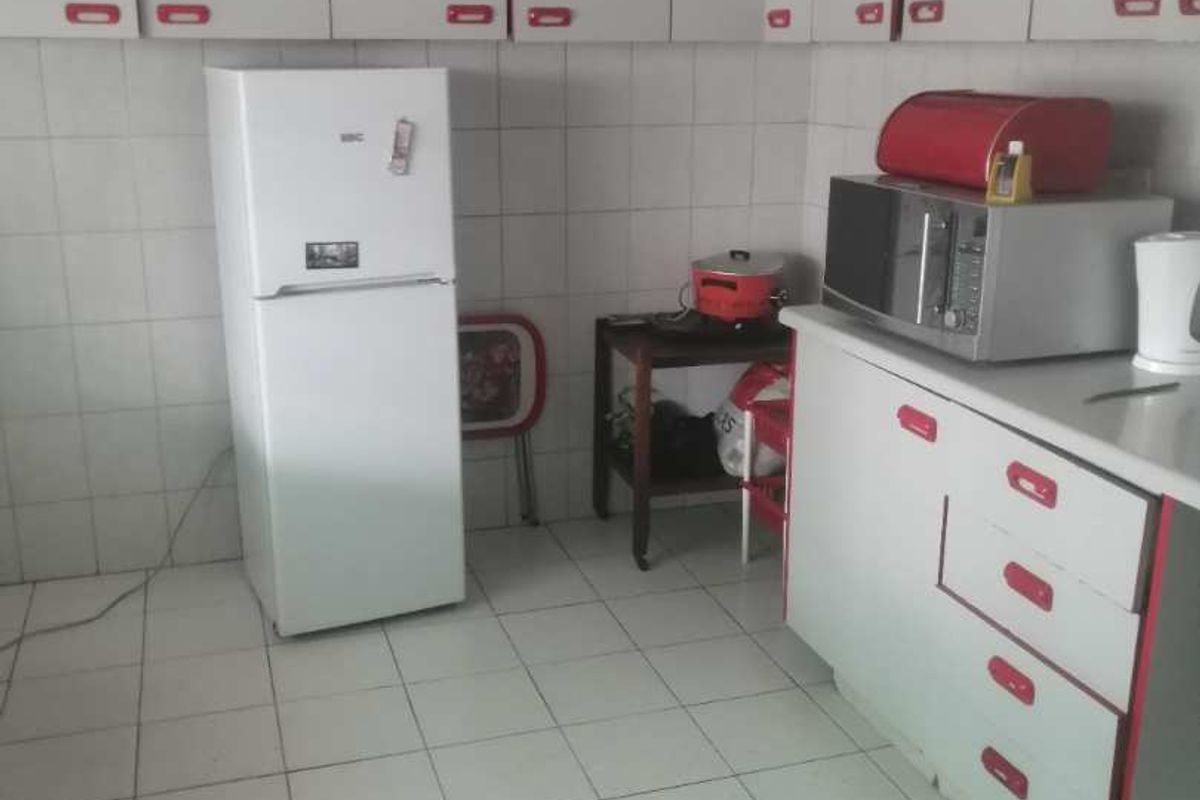 A functional kitchen featuring white cabinetry with red accents, tiled walls, and tiled flooring, providing a basic layout for meal preparation.